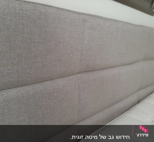 ראש מיטה מרופד בבד אפור ליד מזרן לבן